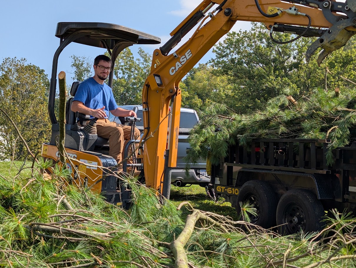 Operating mini excavator to clear pine debris